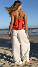 Top de satén color rojo vibrante, con escote pronunciado en V y lazos finos para atar en el frente y en la espalda. Presenta un diseño fruncido en la parte inferior.