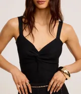 Top cropped negro de tejido de punto texturizado, con tirantes anchos, escote en V y detalle de nudo o torcido en el centro del busto.