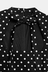 Vestido corto negro con estampado de lunares blancos, cuello redondo con lazada y escote cuadrado. Cuenta con mangas cortas y cierre trasero con cremallera oculta.