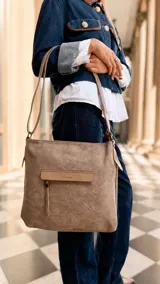 Cartera de tamaño mediano confeccionada en símil cuero color tostado, con diseño de bolsillo frontal con tapa y cierre, correa larga regulable y asa de mano.