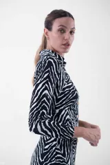 Vestido midi de corte ajustado, con estampado animal print tipo cebra en blanco y negro, cuello camisero, escote en V y cierre frontal con botones dorados.
