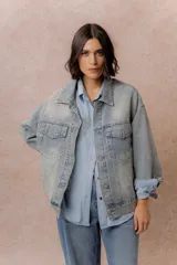 Campera de denim oversized en lavado celeste, con hombros caídos, cierre frontal con botones metálicos, bolsillos delanteros con tapa y aplicaciones de strass con diseño orgánico en delantero, mangas y espalda.