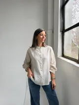 Camisa beige de lino de corte holgado, con cuello mao, mangas largas con puños fruncidos y cierre frontal de botones.