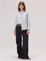 Camisa de algodón con cuello clásico y detalle de volados en la cartera delantera. Presenta mangas largas con puños abotonados y un diseño de corte recto.