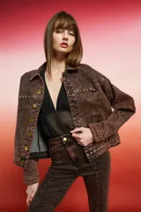 Campera de jean con lavado oscuro rojizo/marrón, estilo trucker. Presenta tachas doradas a lo largo de los bordes de los bolsillos, el canesú y los puños. Posee un bordado en relieve de diseño floral en la manga.