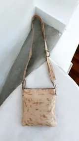 Bandolera de cuero color beige con diseño pintado a mano de flores y arte abstracto, de la marca Carolina De Cunto. Cuenta con correa ajustable y herrajes metálicos color oro viejo.