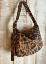 Bolso de hombro tipo hobo con acabado texturizado efecto craquelado en tonos beige y blanco. Cuenta con una correa ajustable con hebilla metálica, cierre superior y diseño espacioso.