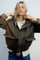 Chaqueta encerada color marrón con efecto lavado, cuello subido y manga larga. Cuenta con bolsillos frontales de plastrón y cierre de cremallera oculto por solapa con botones a presión. Los puños reversibles dejan ver un forro interior con estampado a cuadros.