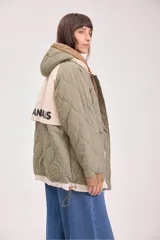 Campera acolchada reversible con capucha, diseño de matelassé, cierre frontal y puños elásticos. Presenta un lado en color verde oliva y otro en color beige.