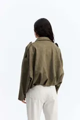 Campera de gamuza sintética color verde oliva, con silueta amplia, hombros caídos y cierre frontal. Presenta un diseño estructurado con volumen en mangas y cuerpo.