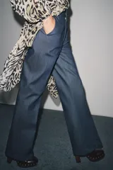 Pantalón de tiro alto confeccionado en algodón, con corte recto y diseño minimalista. Presenta bolsillos laterales, raya planchada en el delantero y cierre frontal con cremallera, botón y ganchos metálicos.