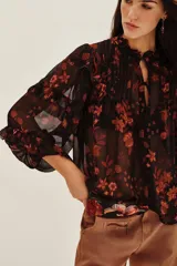 Camisa de viscosa con estampado floral en tonos rojizos y naranjas sobre fondo negro. Presenta volados en los hombros y mangas largas con terminaciones delicadas.