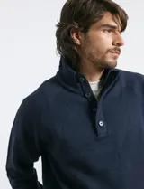 Sweater de punto color azul marino, con cuello alto, cierre frontal parcial y tapeta con botones. Presenta mangas raglán y puños y ruedo acanalados.