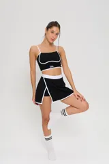 Conjunto deportivo de dos piezas compuesto por un top de tirantes finos con detalle de ribete blanco y logo estampado, y una pollera short con cintura elástica blanca y tajo lateral con ribete blanco.