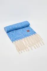 Bufanda rectangular de tejido de punto con textura jaspeada en color azul y flecos largos en color crudo en los extremos. Cuenta con una etiqueta de cuero sintético con logo en una de las esquinas.
