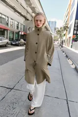Trench de corte oversize color beige, con cuello alto, cierre frontal de botones y mangas largas con puños vueltos estampados a cuadros. Cuenta con bolsillos delanteros de vivo.
