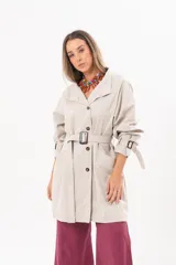 Trench de gabardina Tencel color beige, de silueta relajada, con cierre frontal de botones, lazo desmontable y regulable en la cintura, bolsillos amplios y lazos en los puños.