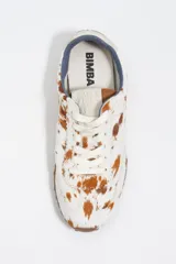 Zapatilla de perfil bajo confeccionada en serraje vacuno con estampado de manchas tipo animal print vacuno. Presenta cierre de cordones, detalle de piel en el talón con logo y suela de goma con textura de tachuelas.