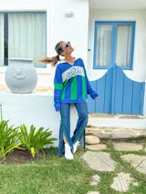 Sweater de punto azul con cuello polo blanco, diseño geométrico en el pecho en blanco y verde, y mangas largas.