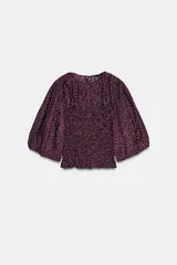 Blusa de color bordó con estampado de lunares claros, confeccionada con cuerpo en nido de abeja elástico, cuello redondo y mangas abullonadas por debajo del codo.