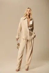 Camisa oversize color beige confeccionada en satén fluido y luminoso, con cuello camisero, mangas largas y puños amplios.