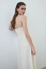 Vestido midi de color blanco con textura arrugada, escote en V, breteles finos y detalle drapeado en el busto.
