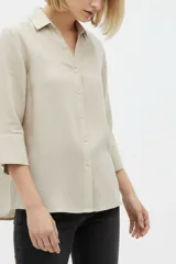 Camisa de algodón color beige, de corte holgado, con mangas tres cuartos, cuello camisero y cierre frontal de botones.