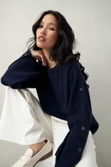 Sweater de tejido de punto color blanco hueso, con cuello redondo y mangas acampanadas. Presenta una hilera de botones a tono en el lateral de cada manga.