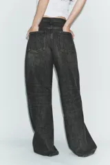Jeans de tiro alto con diseño de pierna ancha y corte extra largo. Presenta una cintura cruzada asimétrica con cierre de cremallera y botones metálicos, además de un diseño clásico de cinco bolsillos.