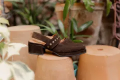 Zapato marrón de gamuza con taco bloque, tira ancha sobre el empeine con apliques metálicos y tira trasera con hebilla.