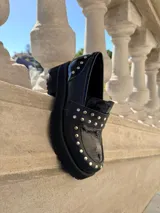 Mocasines de cuero negro con plataforma y suela de goma, decorados con tachas metálicas plateadas en el empeine y el talón.