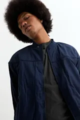 Campera tipo bomber color tostado, con cierre frontal, cuello, puños y ruedo de tejido elástico acanalado. Presenta costuras horizontales en la parte superior del pecho.