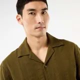 Camisa de manga corta color verde militar, con cuello solapa y cierre frontal de botones. Confeccionada en punto fantasía de algodón con sutiles rayas verticales texturizadas.
