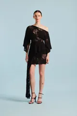 Vestido corto de encaje negro con diseño asimétrico, un hombro al descubierto, mangas amplias y un largo panel lateral colgante.