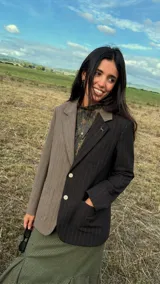 Blazer oversize de diseño bicolor con estructura asimétrica, combinando un lado en tono marrón y otro en negro, ambos con estampado de rayas diplomáticas. Presenta solapas clásicas, cierre frontal con botones de strass y un pin decorativo en forma de perro salchicha en la solapa.
