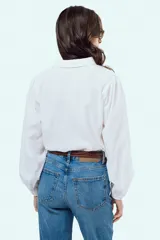 Camisa blanca de manga larga con sutil patrón de rayas verticales, cuello camisero, cierre frontal con botones y puños elásticos.