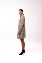 Vestido de punto color beige, de corte holgado y diseño oversized, con cuello alto tipo polera y mangas largas.