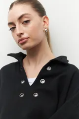 Buzo marrón de algodón con cuello alto y apliques de argollas metálicas.