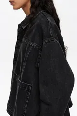 Chaqueta corta de corte línea A confeccionada en mezcla de algodón color negro. Presenta cuello camisero, mangas largas con botones, bolsillos delanteros tipo plastrón y canesú con maxi pliegue en la espalda.