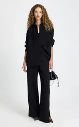 Pantalon sastrero negro de corte recto y tiro alto. Presenta cintura elástica con cordón ajustable, bolsillos laterales con ribete en contraste, pespuntes decorativos y aberturas laterales en el bajo.