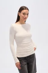 Top de manga larga ajustado al cuerpo, color beige claro, con escote bote y detalle de frunces drapeados en el torso.