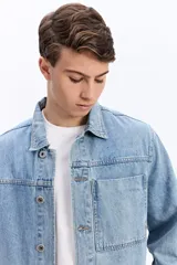Campera de jean de corte recto y lavado desgastado, con cuello clásico, cierre frontal con botones metálicos y un bolsillo grande aplicado en el pecho.