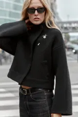Chaqueta estilo bomber de punto color negro, con cuello subido, manga larga y cierre frontal cruzado con botones ocultos a presión. Presenta bolsillos delanteros de vivo.