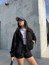 Campera tipo bomber de tela scuba con textura de gamuza, color negro, con cierre frontal, bolsillos laterales y puños elásticos.