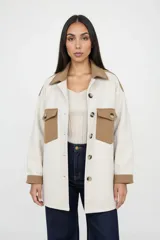 Sobre camisa de corte oversize en combinación de colores natural y camel. Presenta cuello clásico, cierre frontal con botones, mangas largas con puños en contraste y dos bolsillos frontales con solapa y botón.