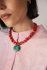 Collar corto compuesto por cuentas de cristal checo en tonos rojos de diversas formas y tamaños, con un medallón central circular de cristal checo en color verde. Incluye cadena de ajuste para regular el largo.