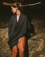 Ruana de tejido abierto en color negro con destellos brillantes plateados, de diseño envolvente y caída fluida.