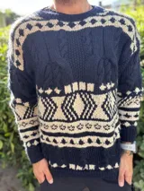 Buzo de tejido de punto grueso con diseño de guardas geométricas en colores azul marino y crudo. Presenta cuello redondo, mangas largas y puños acanalados.