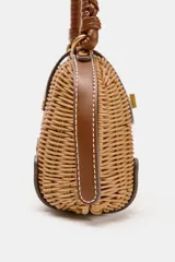Bolso rígido tipo bandolera de mimbre trenzado en tono natural, con detalles en cuero sintético marrón, asa superior trenzada y cierre metálico dorado.