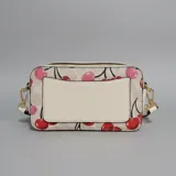 Cartera tipo bandolera de formato rectangular con estampado de cerezas sobre fondo claro. Cuenta con cierre superior, tirador con flecos y correa de tela ajustable y extraíble.